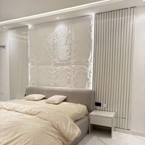 Snowflake White PU faux stone panels installed behind a bed with fluted wall panels