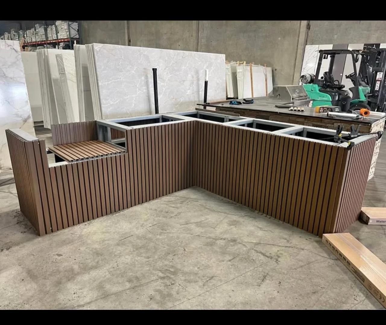 Outdoor kitchen island under construction with teak and black slat cladding installed around the exposed frame